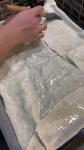 Brushing the vinegar sauce onto a sheet of yufka.