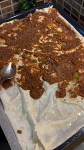 Spreading ground beef topping thinly over a yufka sheet.