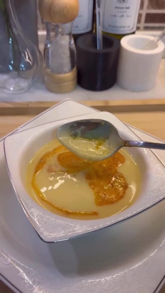 A bowl of creamy ivory-colored Çeşmi Nigar soup with a red pepper butter drizzle.