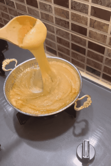 A copper pan filled with bubbling Muhlama and a wooden spoon lifting the stretchy cheese.