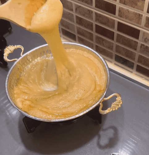 A copper pan filled with bubbling Muhlama and a wooden spoon lifting the stretchy cheese.