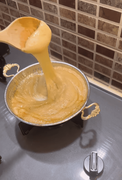 A copper pan filled with bubbling Muhlama and a wooden spoon lifting the stretchy cheese.
