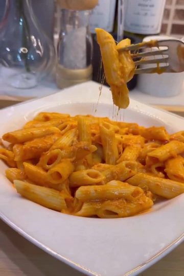 A bowl of penne pasta coated in a vibrant, creamy orange pepper paste sauce.