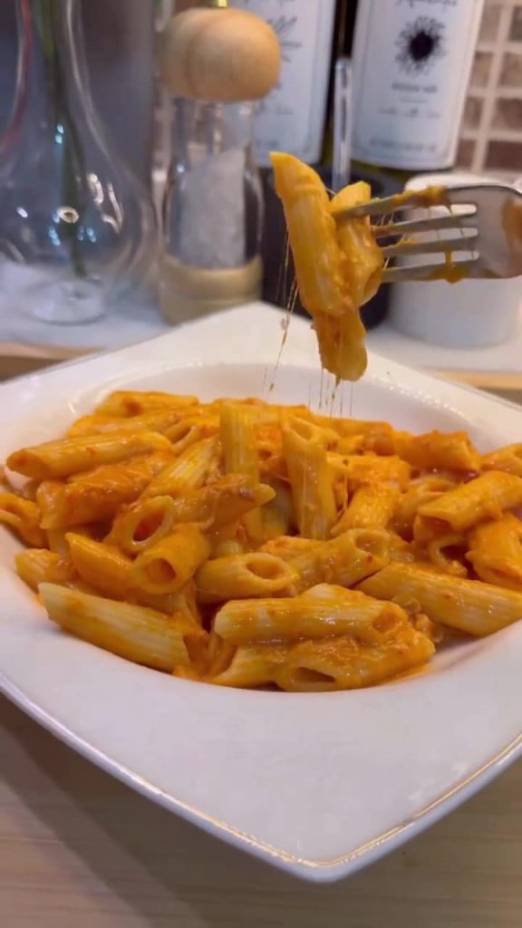 A bowl of penne pasta coated in a vibrant, creamy orange pepper paste sauce.