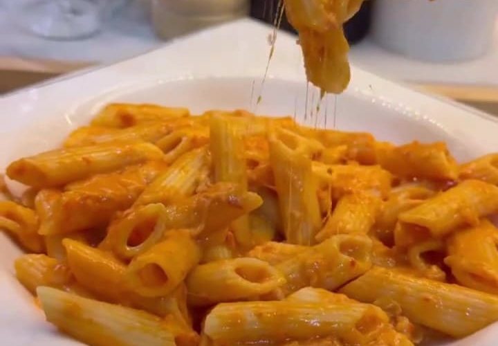 A bowl of penne pasta coated in a vibrant, creamy orange pepper paste sauce.