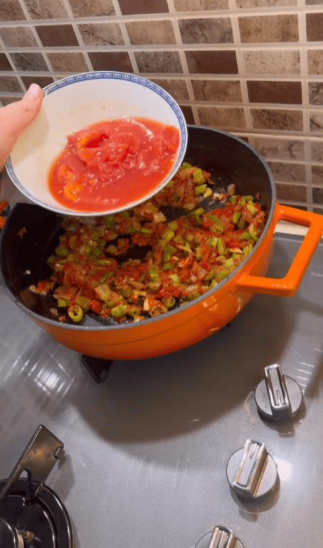 Mixing fresh diced tomatoes into a savory sauce base.