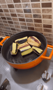 Searing whole eggplant pieces in a skillet with vegetable oil.