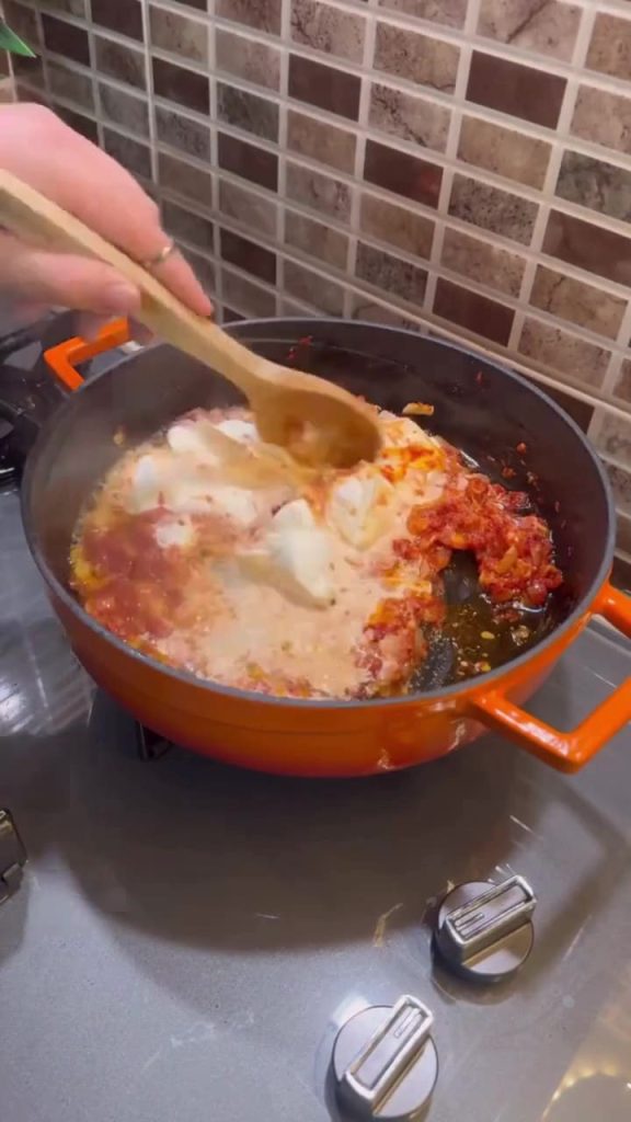Pouring heavy cream into a red pepper paste base.