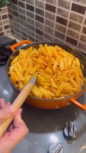 Tossing boiled pasta into a creamy red sauce.