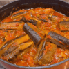 A pot of seared eggplants simmered in a vibrant red tomato and pepper sauce.