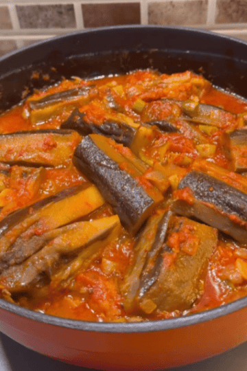 A pot of seared eggplants simmered in a vibrant red tomato and pepper sauce.