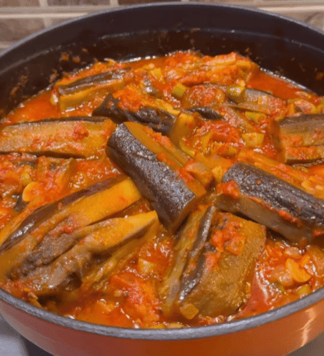 A pot of seared eggplants simmered in a vibrant red tomato and pepper sauce.