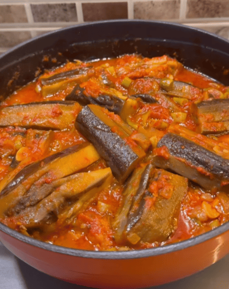 A pot of seared eggplants simmered in a vibrant red tomato and pepper sauce.