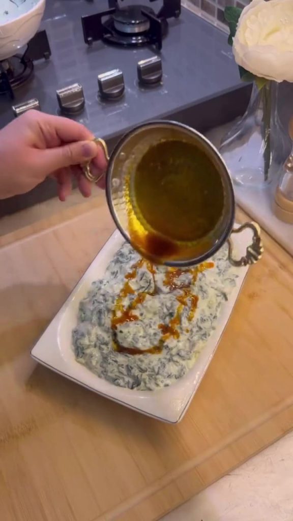 Pouring red pepper butter over a Turkish spinach meze.