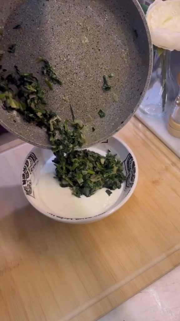 Mixing sautéed spinach into creamy garlic yogurt.