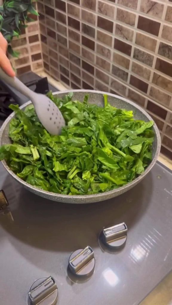Sautéing spinach and onions in a skillet.