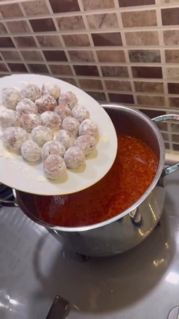 Dropping flour-coated meatballs into a boiling red stew.