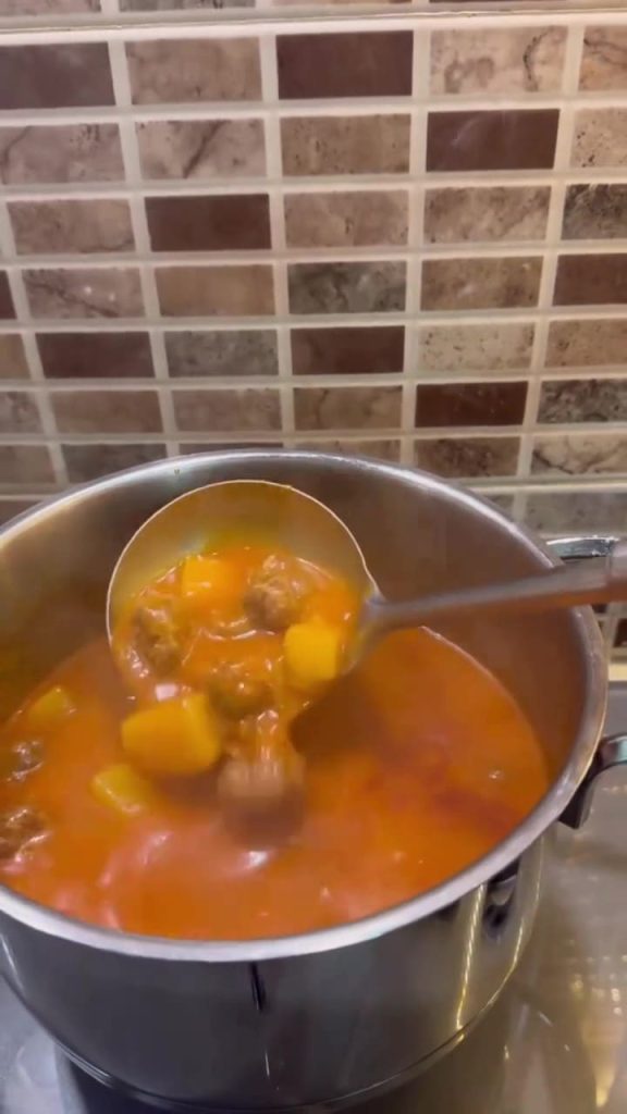 A bubbling pot of Turkish meatball and potato stew on a stovetop.