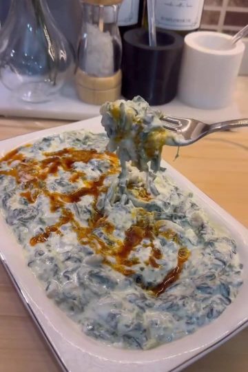 A bowl of creamy spinach borani topped with a bright red pepper butter drizzle.