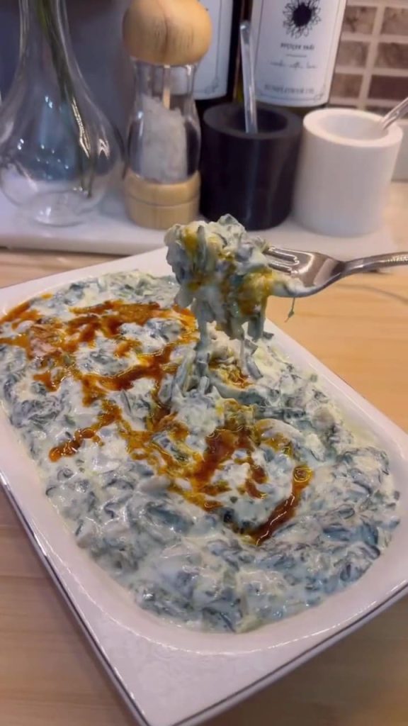 A bowl of creamy spinach borani topped with a bright red pepper butter drizzle.