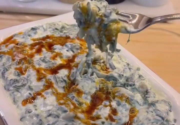 A bowl of creamy spinach borani topped with a bright red pepper butter drizzle.